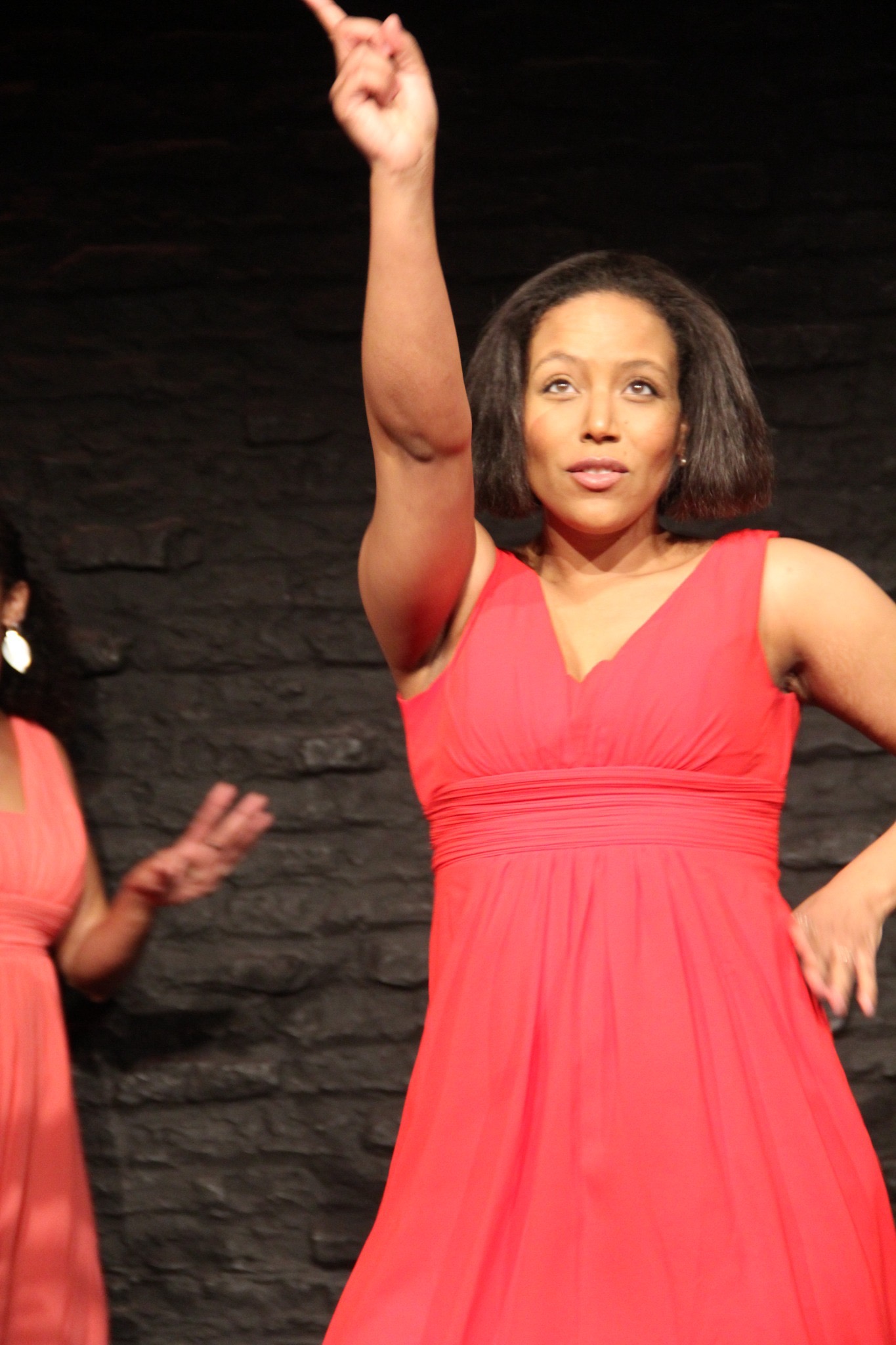 A woman in coral pointing upward in a moment of self-recognition.