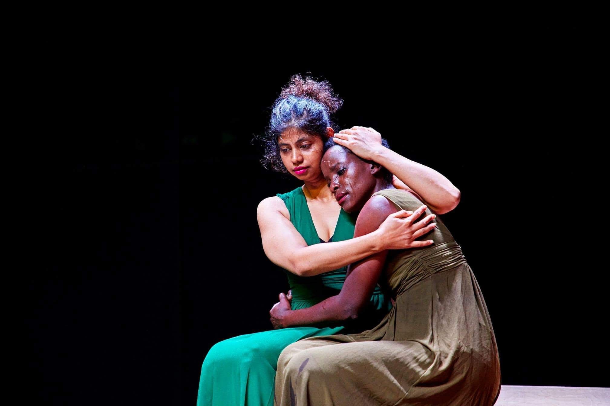 Two women in green and brown in a close embrace.