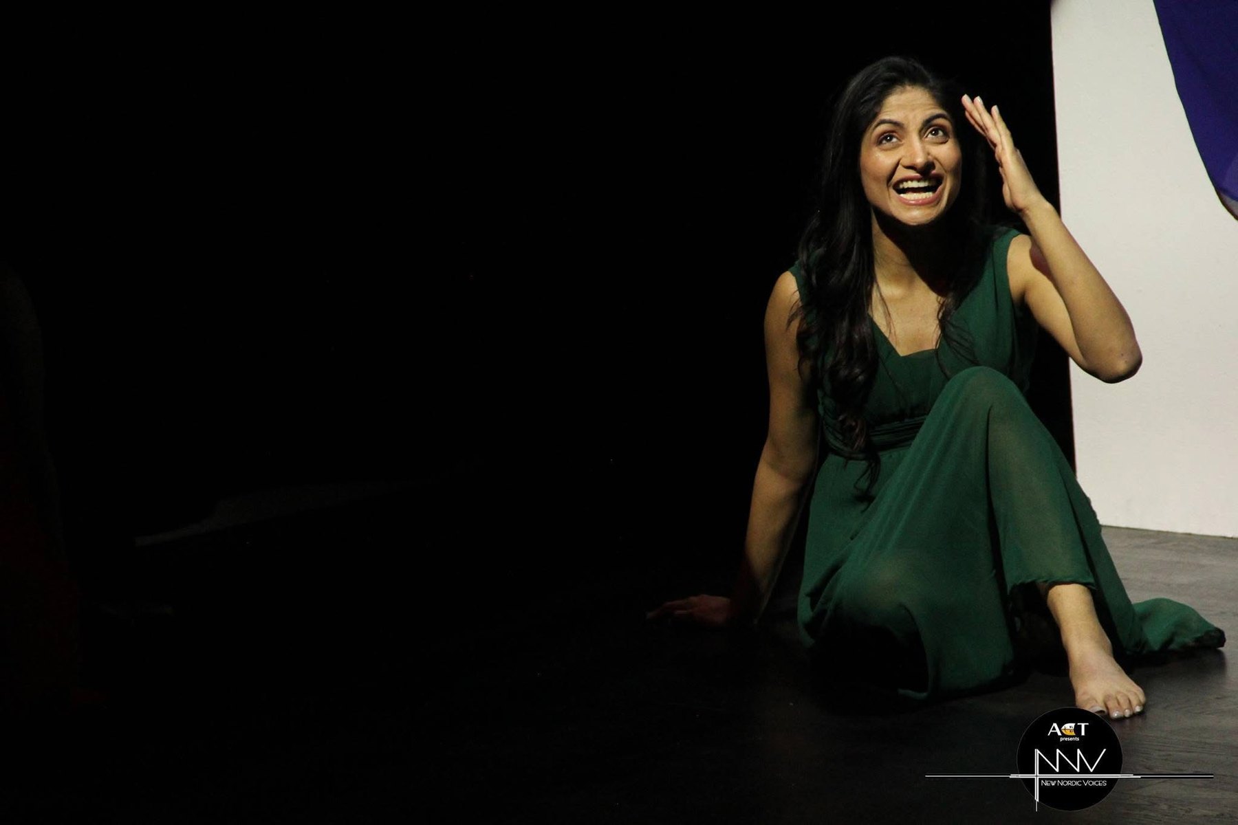 A performer in green seated in a poised solo moment.
