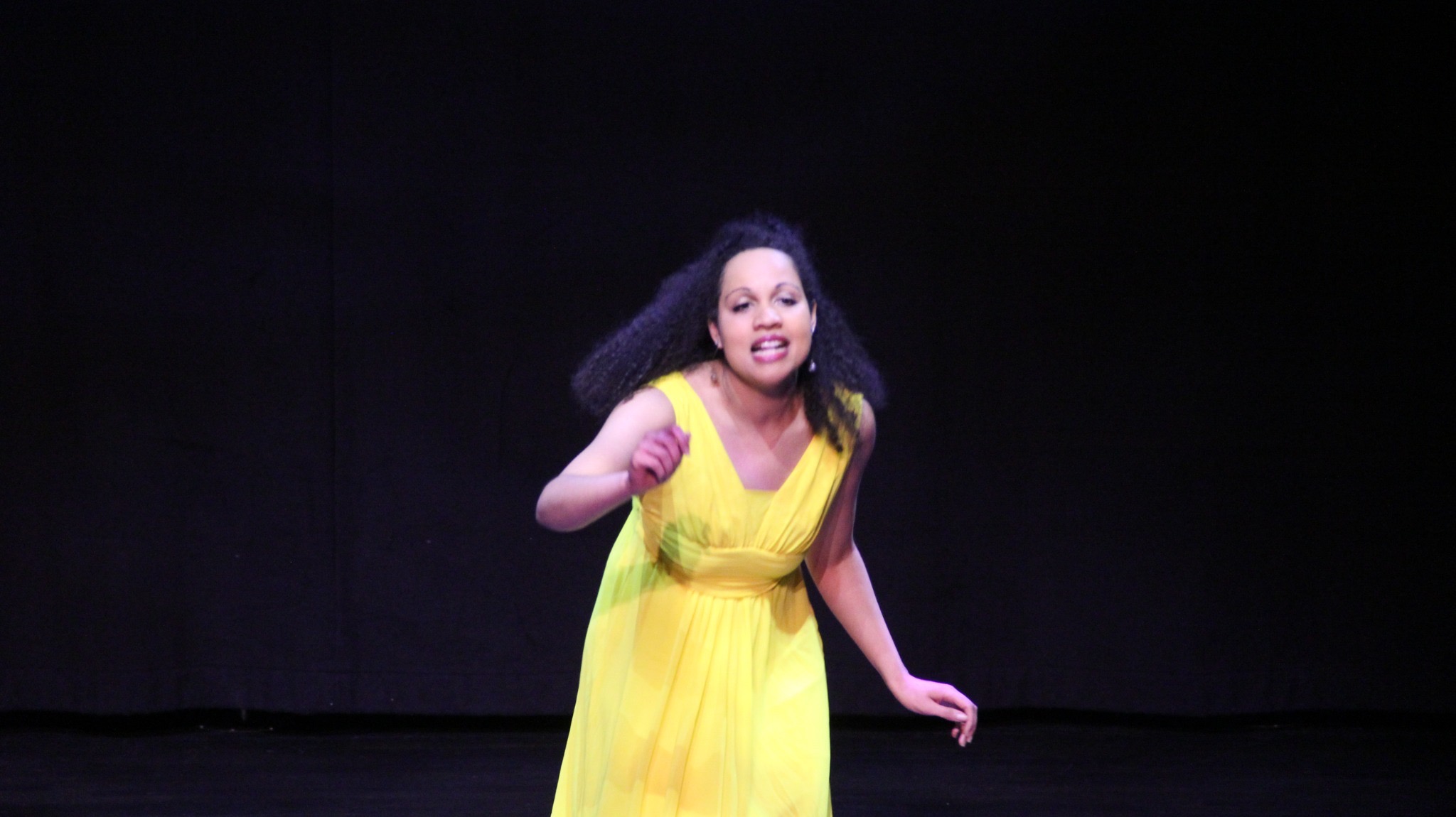 A performer in yellow leaning forward in a vivid solo moment.