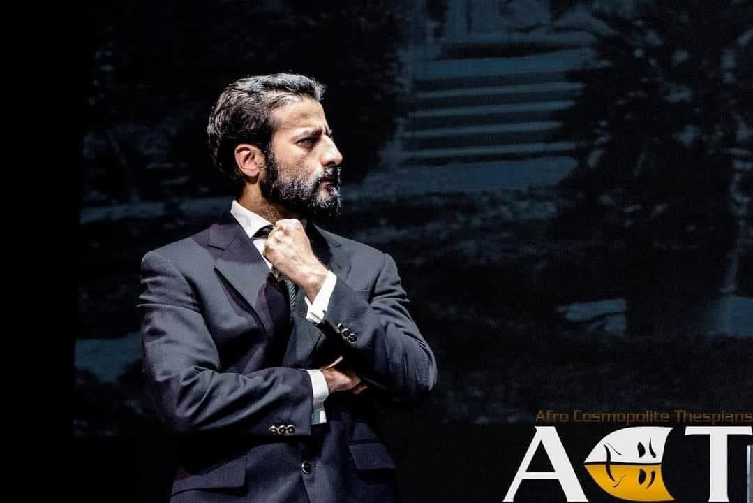 Antonio standing alone in a tailored suit in The Merchant of Venice.
