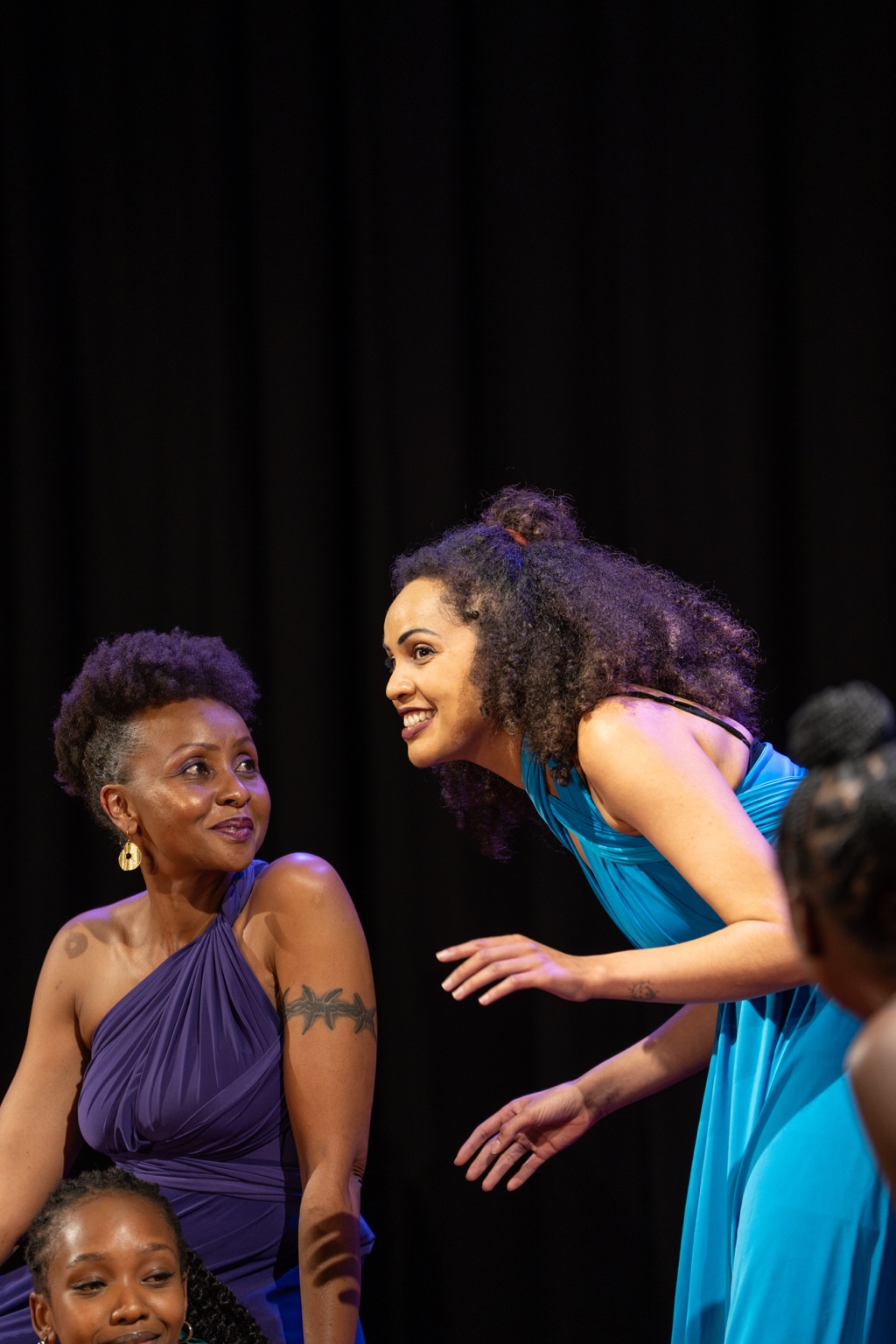 Two performers in blue and purple sharing an intimate stage exchange.