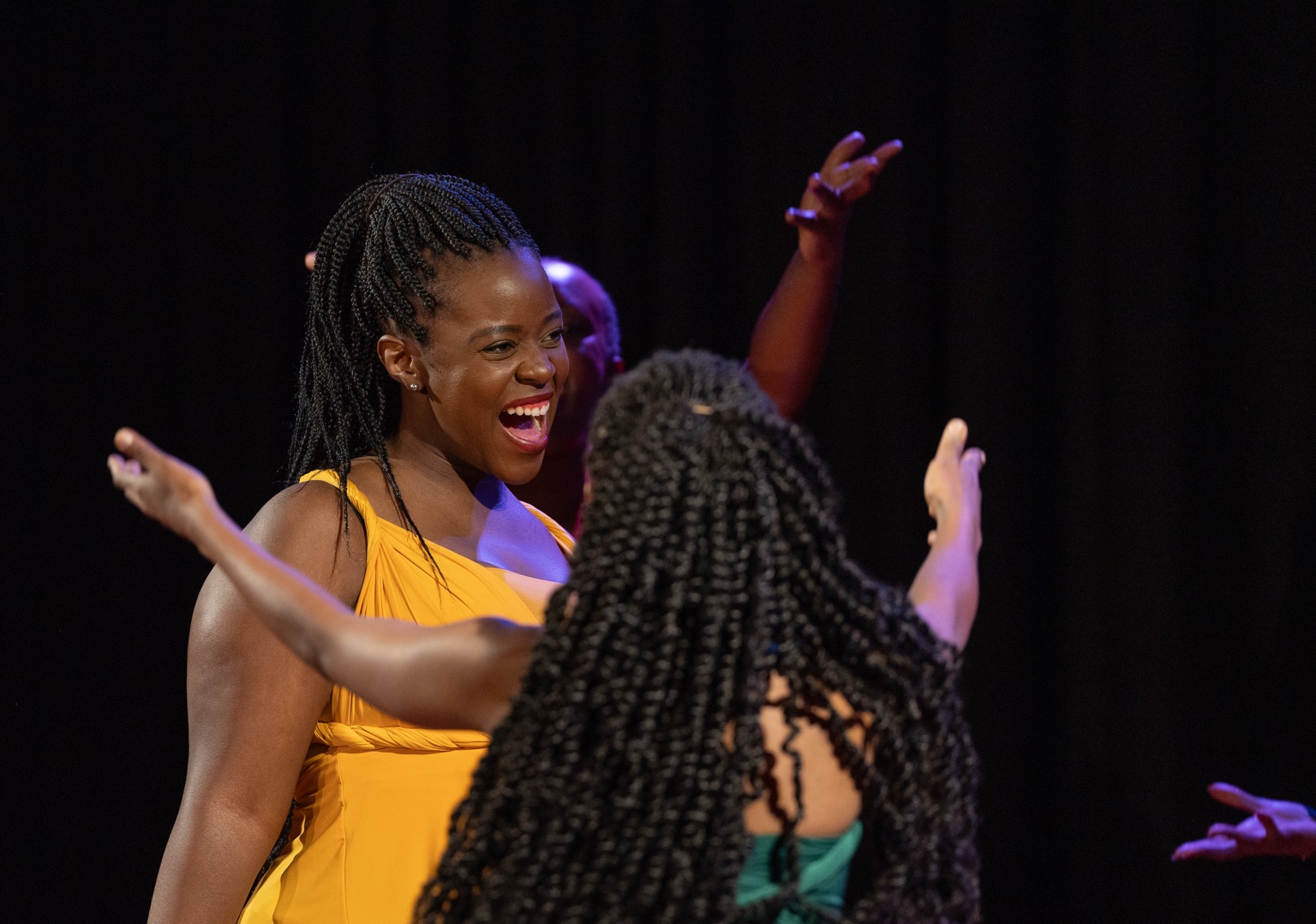 A performer in yellow laughing as the ensemble gathers around her.