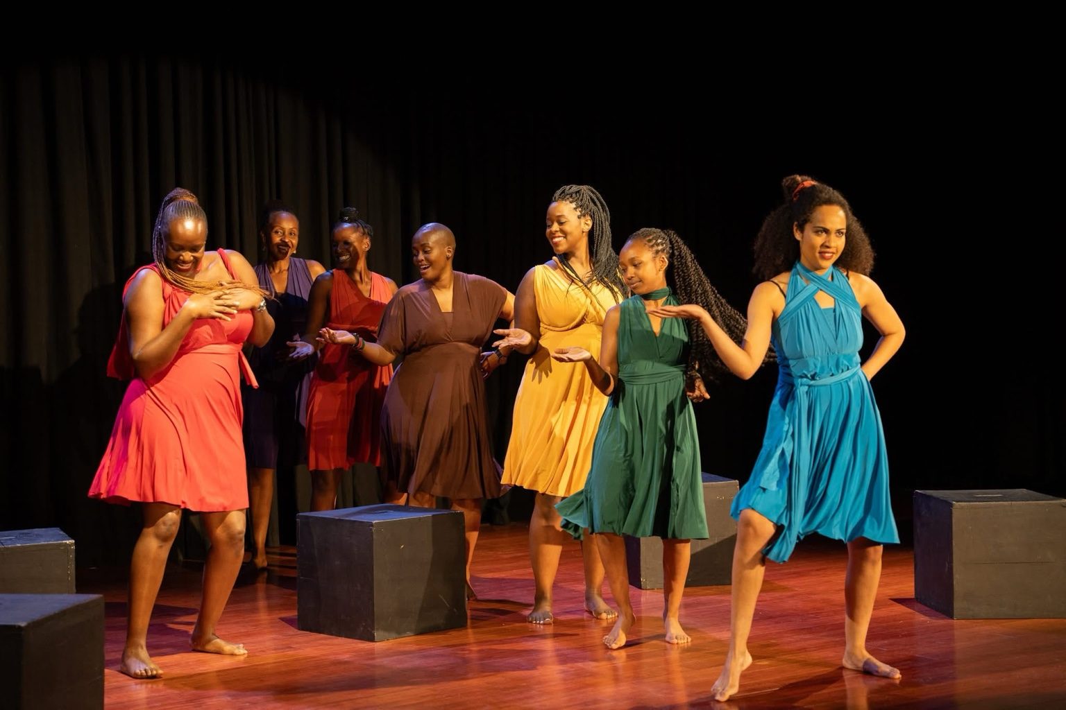 The ensemble moving across the stage in colored dresses.